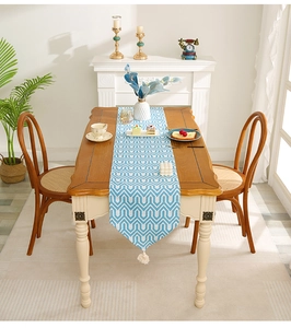 Close-up of blue geometric table runner with white tassels on a rustic wood dining table