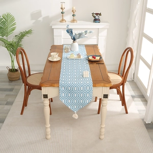 Minimalist blue wave pattern table runner with white tassels on a rustic wood table