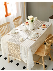 Detail of light brown geometric table runner with tassels over white lace tablecloth