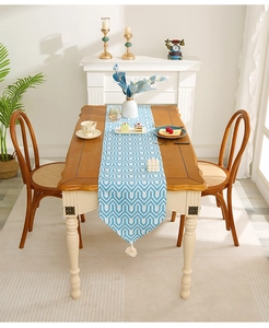 Close-up of blue geometric wave pattern table runner with creamy white tassels on wood