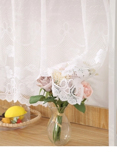 Detailaufnahme weißer Blumenstickerei aus Spitze auf transparentem Kaffeevorhang