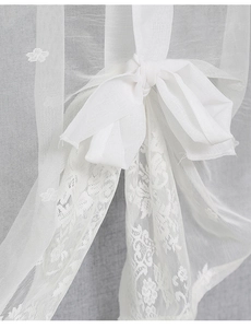 Close-up of white lace curtain fabric featuring floral embroidery and decorative bow tie