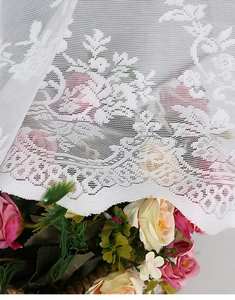 Close-up of white lace curtain fabric showing intricate rose patterns and scalloped edges