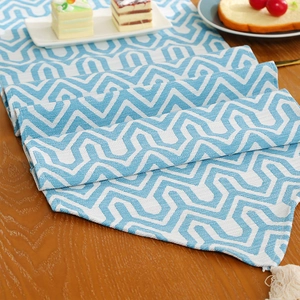 Modern blue and white geometric table runner with tassels on a wooden dining table