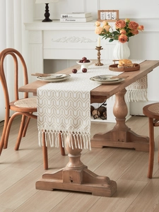 Close-up of beige jacquard table runner with wave pattern and tassels on wood table
