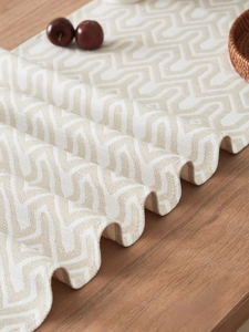 Detailed view of beige jacquard table runner with geometric weave on wooden table