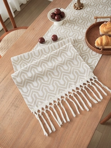 Close-up of geometric jacquard table runner with decorative fringe tassels on wood