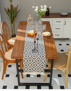 Detail of grey geometric table runner with white tassels on a modern wooden dining table