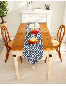 Detail of blue geometric table runner with white tassels on a wooden dining table