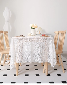 Detail of white lace tablecloth featuring elegant floral hollow embroidery on a wooden table