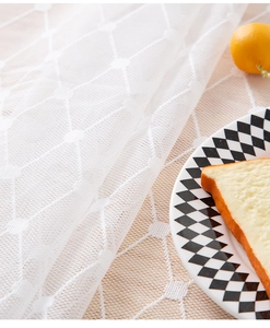 Close-up of white lace tablecloth with geometric diamond mesh patterns and breakfast set
