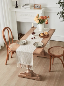 Dettaglio della runner da tavola jacquard beige con frange su un tavolo di legno