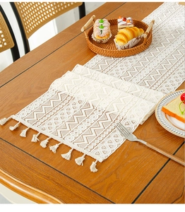 Detailed view of white geometric lace table runner with elegant fringe tassels on wood