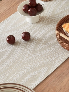 Dettaglio del runner da tavola in cotone e lino con motivi a foglie beige intrecciate