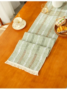 Close-up of green woven table runner with jacquard texture and beige tassels on wood