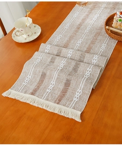 Detail of khaki linen table runner with white woven stripes and fringe on wooden table