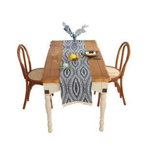 Blue linen table runner with white leaf patterns and fringe on a wooden dining table