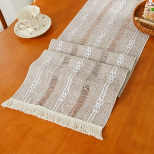 Modern woven table runner with white wave patterns and tassels on a wooden tea table