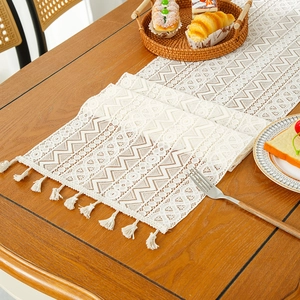 Camino de mesa de encaje beige con diseño de ganchillo y borlas en mesa de comedor de madera