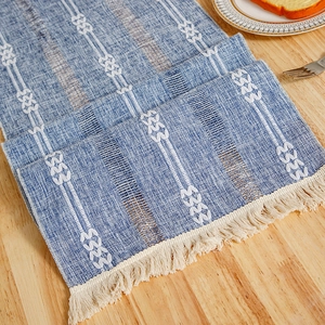 Blue and white geometric table runner with tassels on a wooden dining table