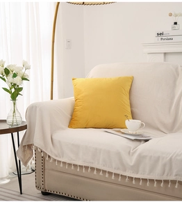 Detail of a mustard yellow velvet cushion on a cozy sofa with fringe throw and floral decor