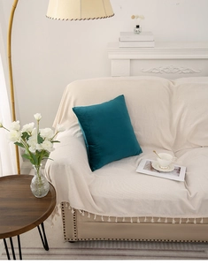 Close-up of teal velvet quilted throw pillow placed on a modern beige fabric sofa