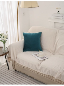 Detail of dark teal velvet throw pillow on a beige sofa with warm cozy home decor