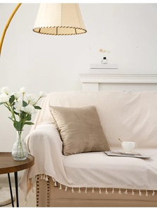 Detail of cream tassel sofa throw with brown velvet pillow in a cozy living room scene
