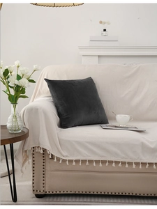 Detail of beige tasselled sofa throw and dark grey velvet pillow in home setting