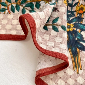 Detailed close-up of checkered silk scarf with green floral pattern and red-brown edge