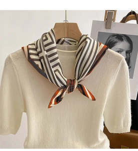 Close-up of geometric silk scarf in orange and cream styled on a white knitted sweater