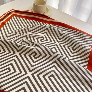 Close-up of silk square scarf with Greek key pattern and orange border on white desk