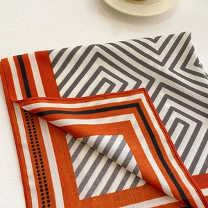 Detail of geometric twill silk scarf showing intricate orange and black spiral patterns