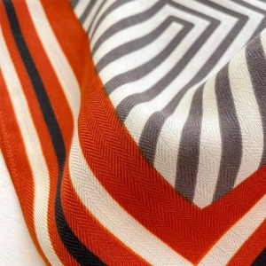 Macro shot of geometric pattern silk scarf showing detailed orange and black woven texture