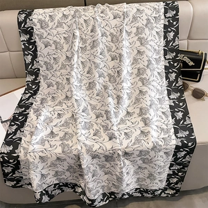 Eleganter Seidenschal mit Blumenmuster in Schwarz-Weiß auf Sofa mit Mode-Accessoires