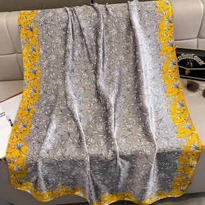 Eleganter Seidenschal mit Lilienprint und gelbem Rand auf einem grauen Ledersofa