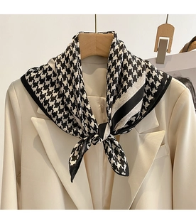 Close-up of a black and white houndstooth silk scarf tied on a beige suit blazer collar