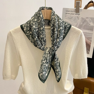 Floral dark green silk square scarf tied on neck over a beige knit shirt