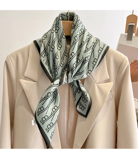 Detail of mint green silk scarf with monogram print worn on a beige blazer lapel
