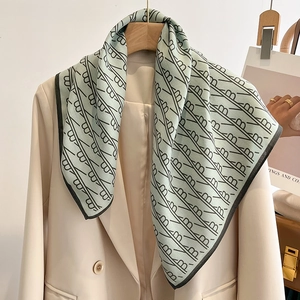 Detailed view of mint green silk scarf with black B-letter pattern on beige blazer