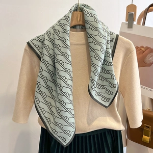 Mint green square scarf with black geometric patterns styled on a wooden hanger