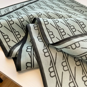 Detailed close-up of light green knit scarf featuring black letter B patterns and hemmed edges