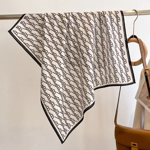 Detail of silk scarf with black and white monogram pattern hanging on a metal rack