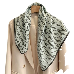 Mint green fashion scarf with letter patterns draped on a beige blazer hanger