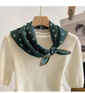 Close-up of a dark green silk scarf with white leaf patterns on a white knit shirt