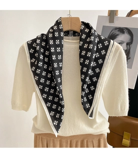 Detail view of a black and white geometric silk scarf paired with a beige knit top