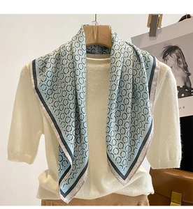 Detail of light blue silk scarf with green chain patterns and contrast edging on a hanger