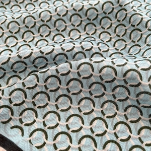Detailed close-up of light blue silk scarf with green and pink chain print and twill weave