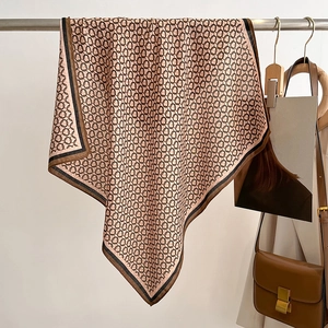 Detail of pink silk scarf with chain print and black contrast border on a wooden hanger