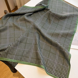 Detail of green and black houndstooth pattern on fine knit scarf and stitched edges